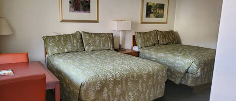 A hotel room with two beds, a desk, a chair, and two framed pictures on the wall.