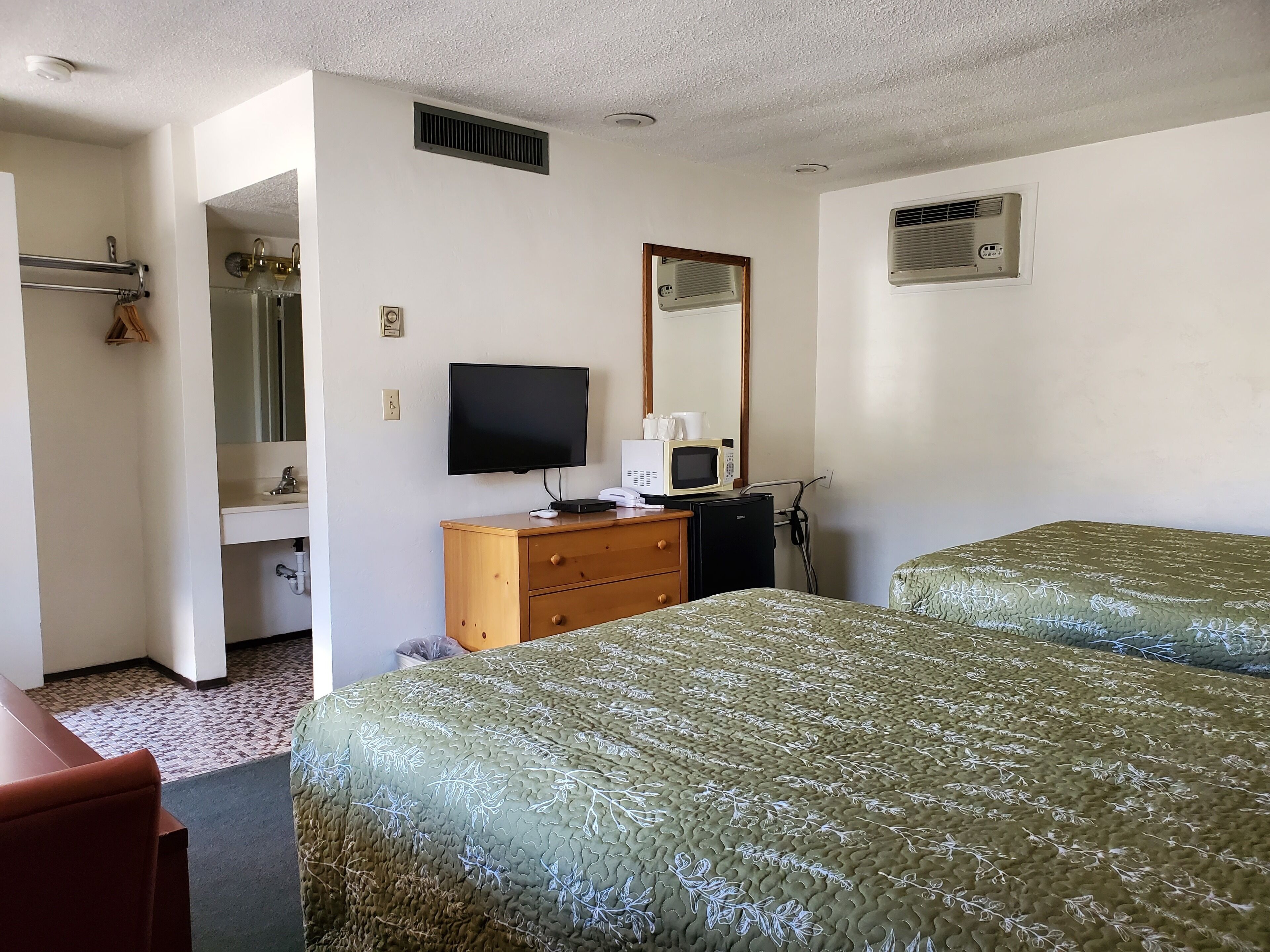 Habitación de hotel con dos camas, televisión, microondas, cómoda, espejo y baño con toallero y lavamanos.