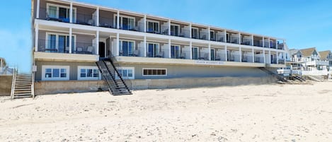 A multi-story motel with balconies, a staircase leading to the entrance, and a beach view.