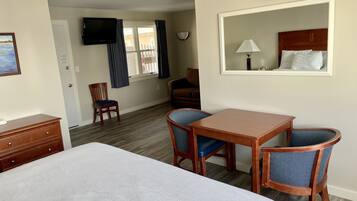 Habitación de hotel con cama, escritorio, dos sillas, televisor, ventana con cortinas y espejo.