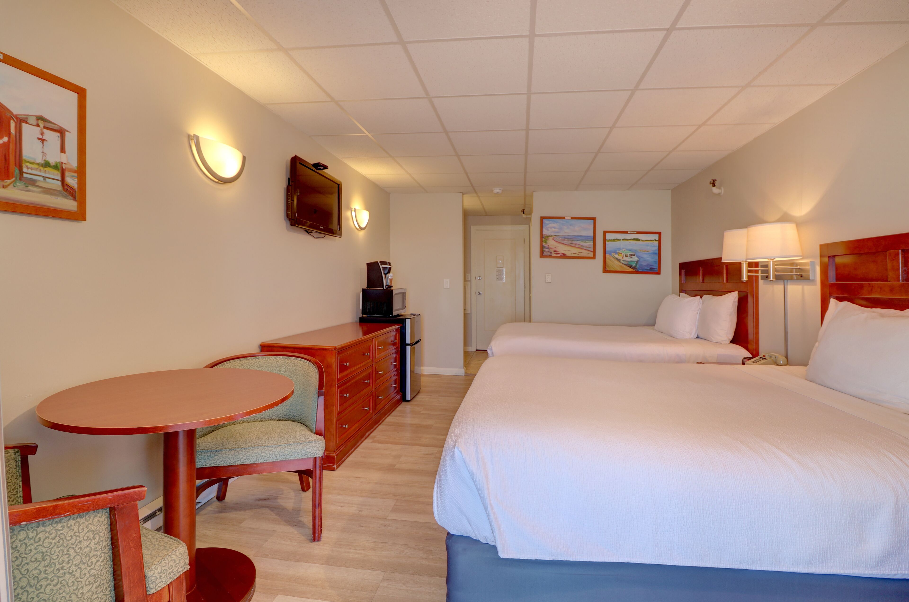 A hotel room with two beds, a desk with a chair, a dresser, and a small table.