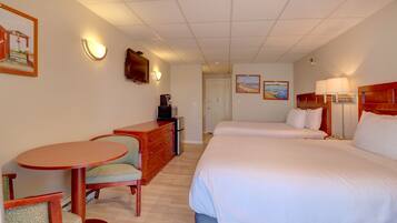 A hotel room with two beds, a desk with a chair, a dresser, and a small table.