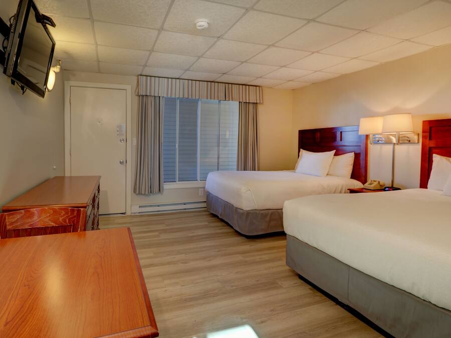 Quarto de hotel com duas camas, uma escrivaninha de madeira, televisão e janela com cortinas.
