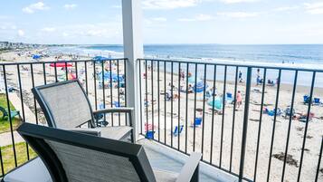 Ein Balkon mit Blick auf einen Strand, ausgestattet mit Stühlen und einem Tisch.