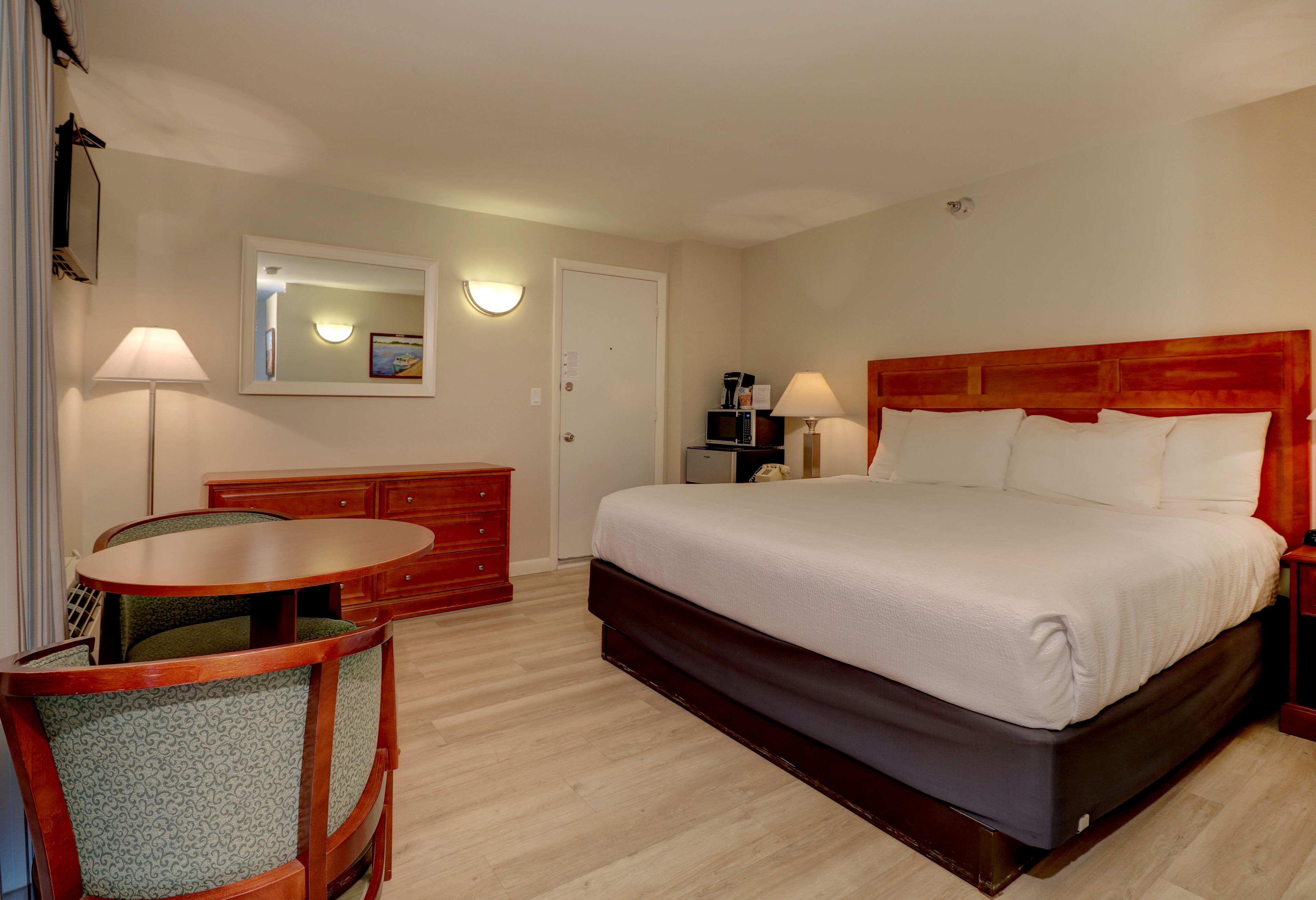 A hotel room with a bed, a desk, a chair, a dresser, and a mirror.