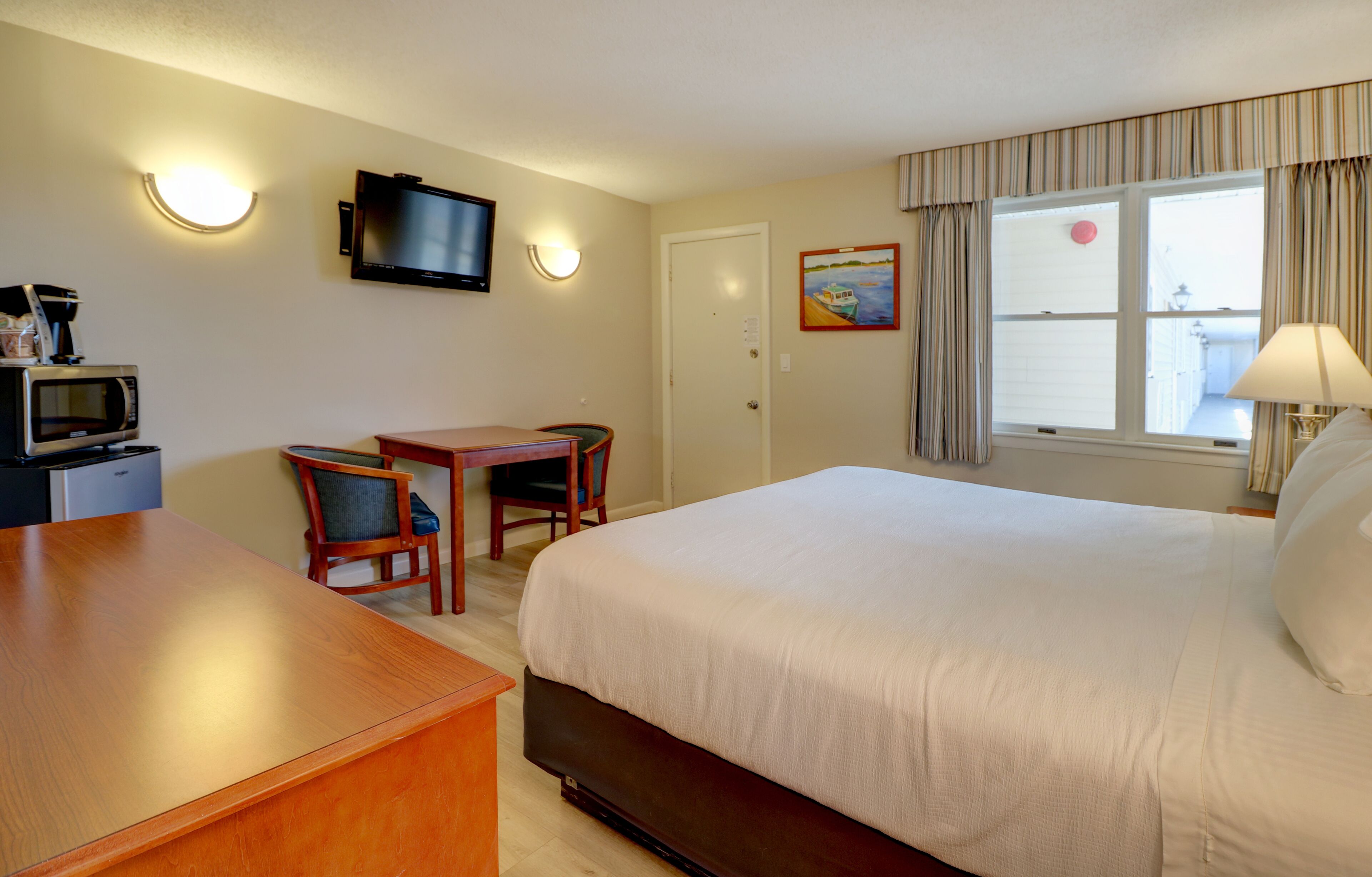 Een hotelkamer met een groot bed, een bureau met een stoel, een televisie en een raam met gordijnen.