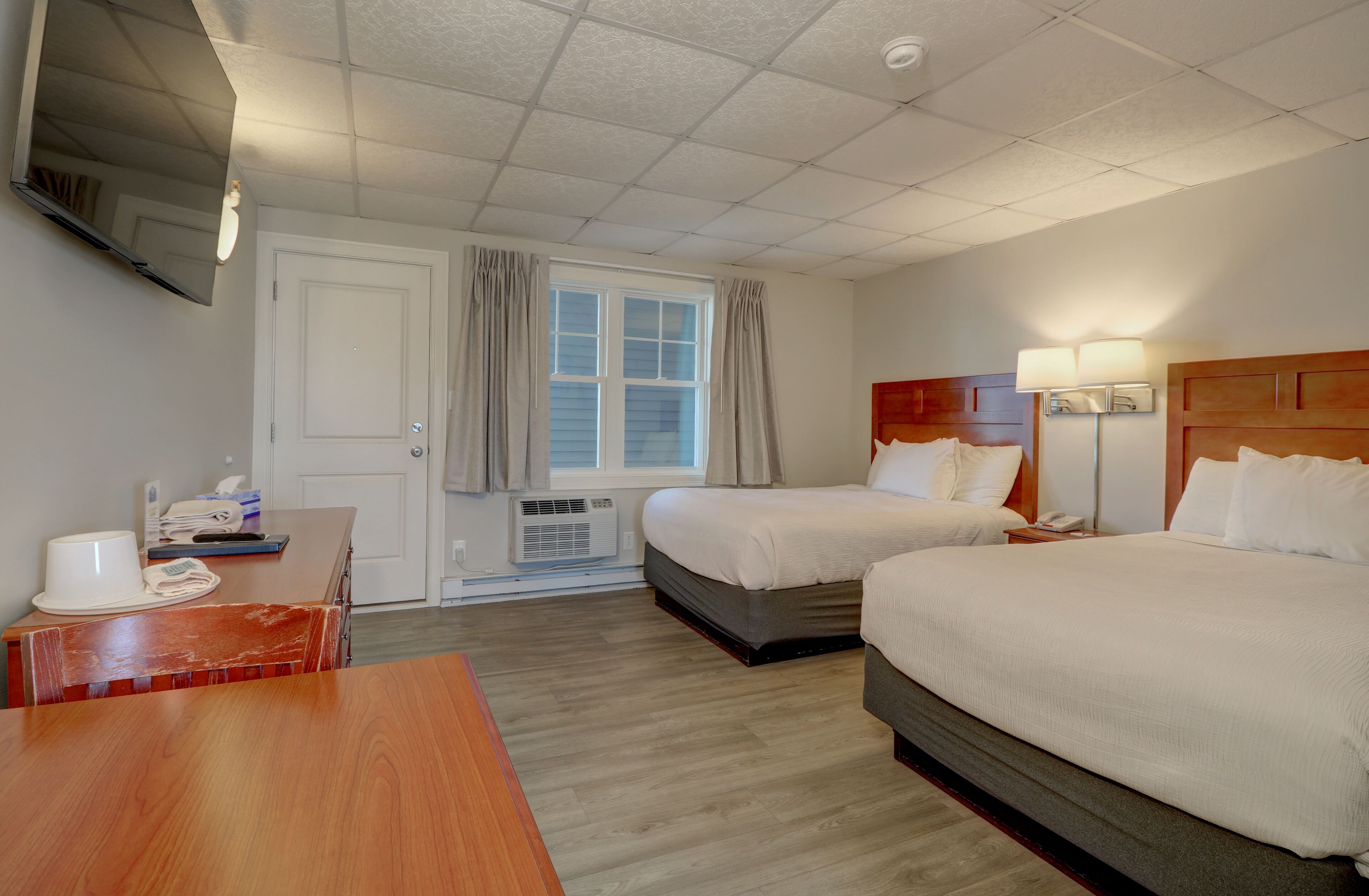 Habitación de hotel con dos camas, un escritorio, un televisor montado en la pared y una ventana con cortinas.