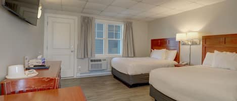 Habitación de hotel con dos camas, un escritorio, un televisor montado en la pared y una ventana con cortinas.