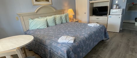 Un dormitorio con cama, escritorio, silla, televisor y refrigerador.