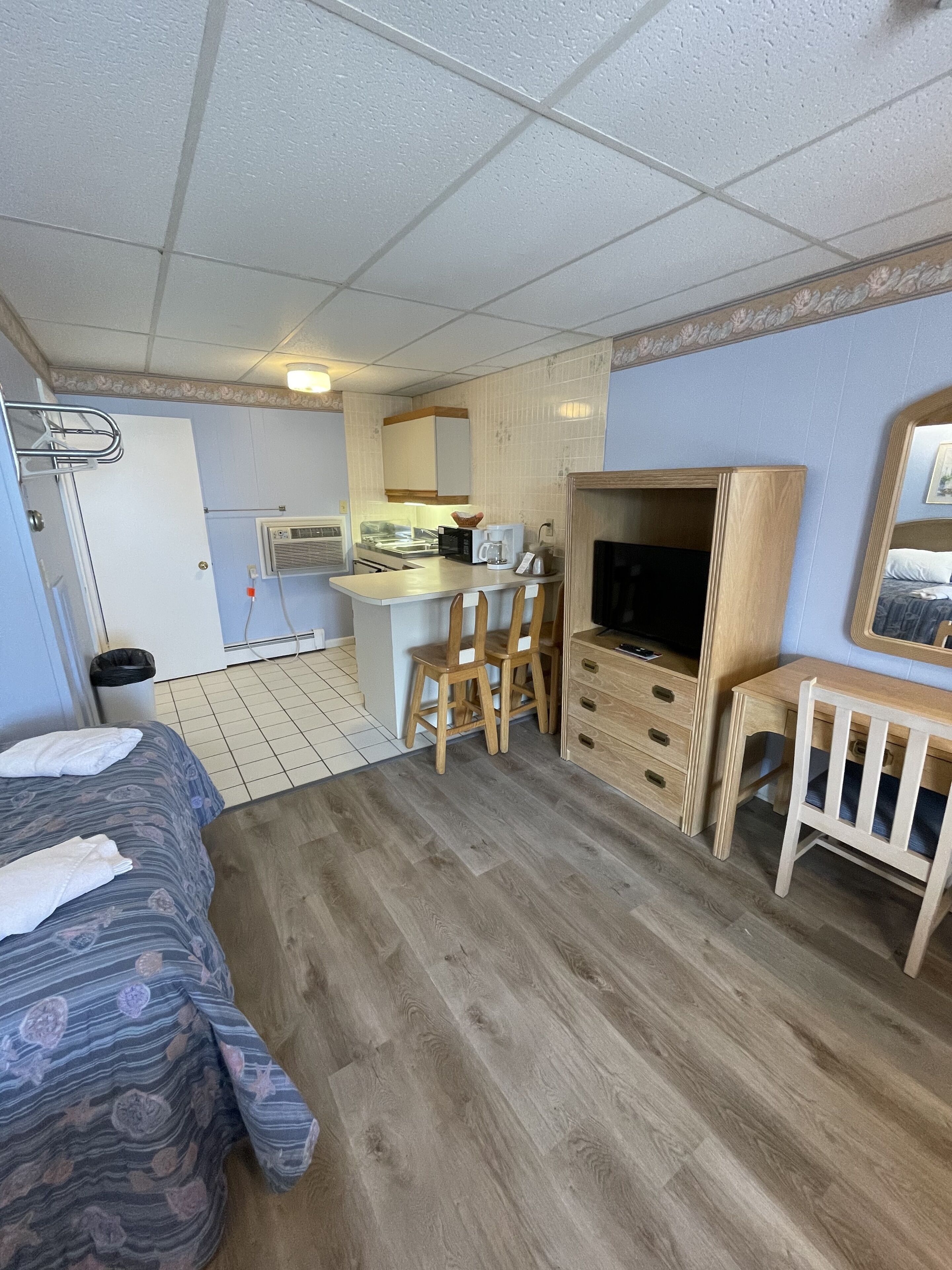 A compact room with a bed, a small kitchenette, a TV, and a desk.