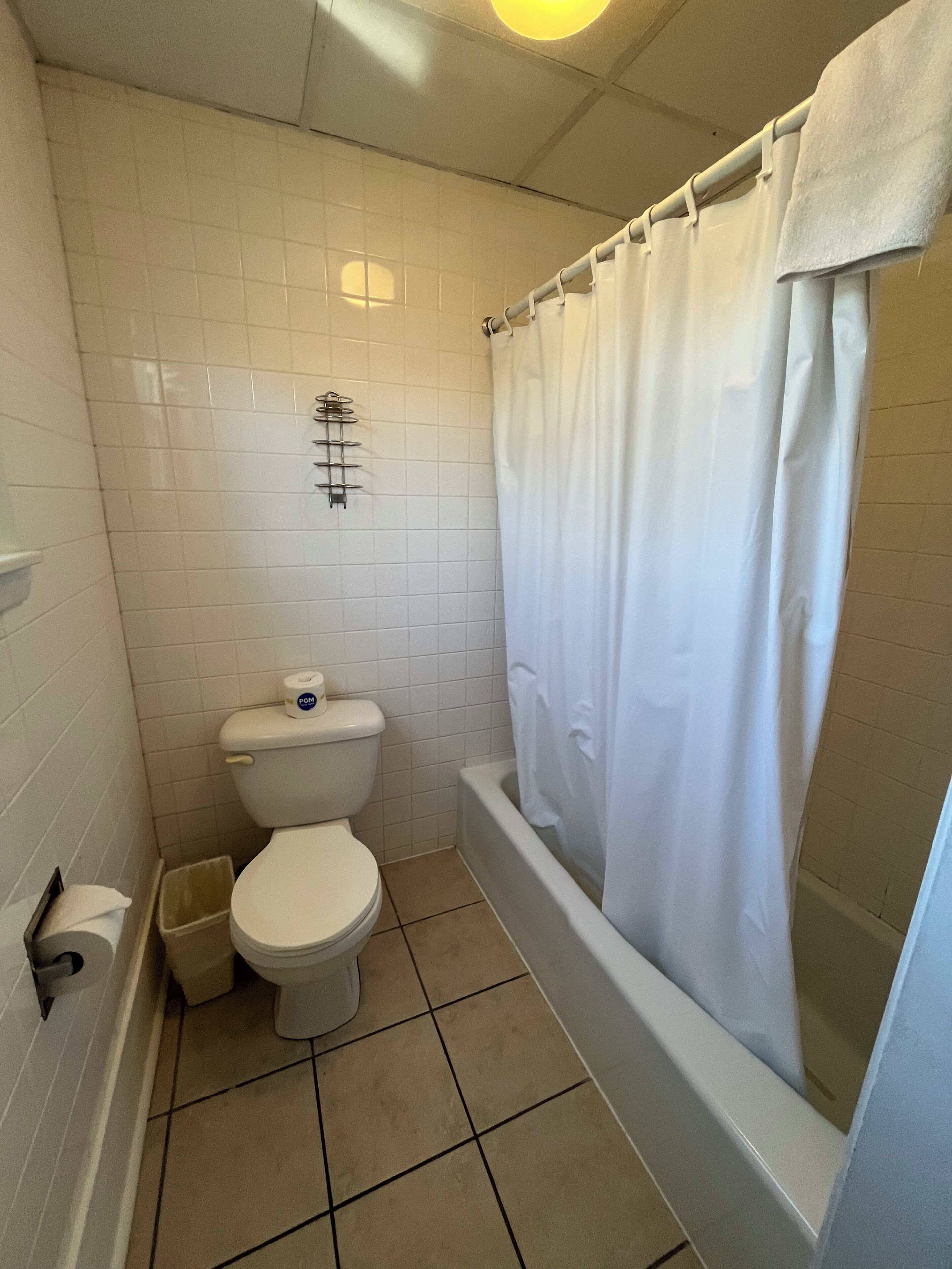 A small, clean bathroom with white tiles, a toilet, a bathtub, and a shower curtain.