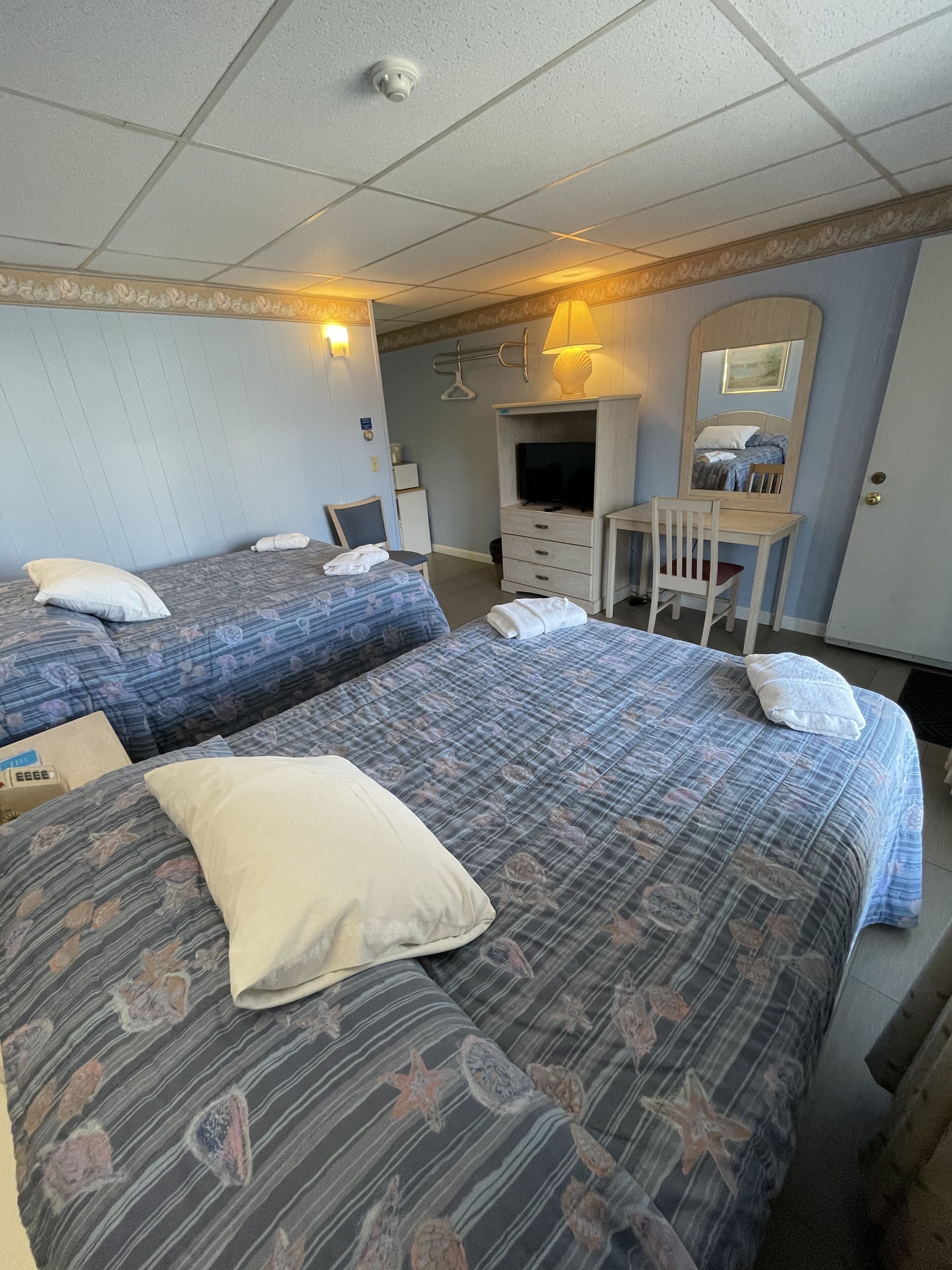 A hotel room with two beds, a desk, a chair, a television, and a mirror.