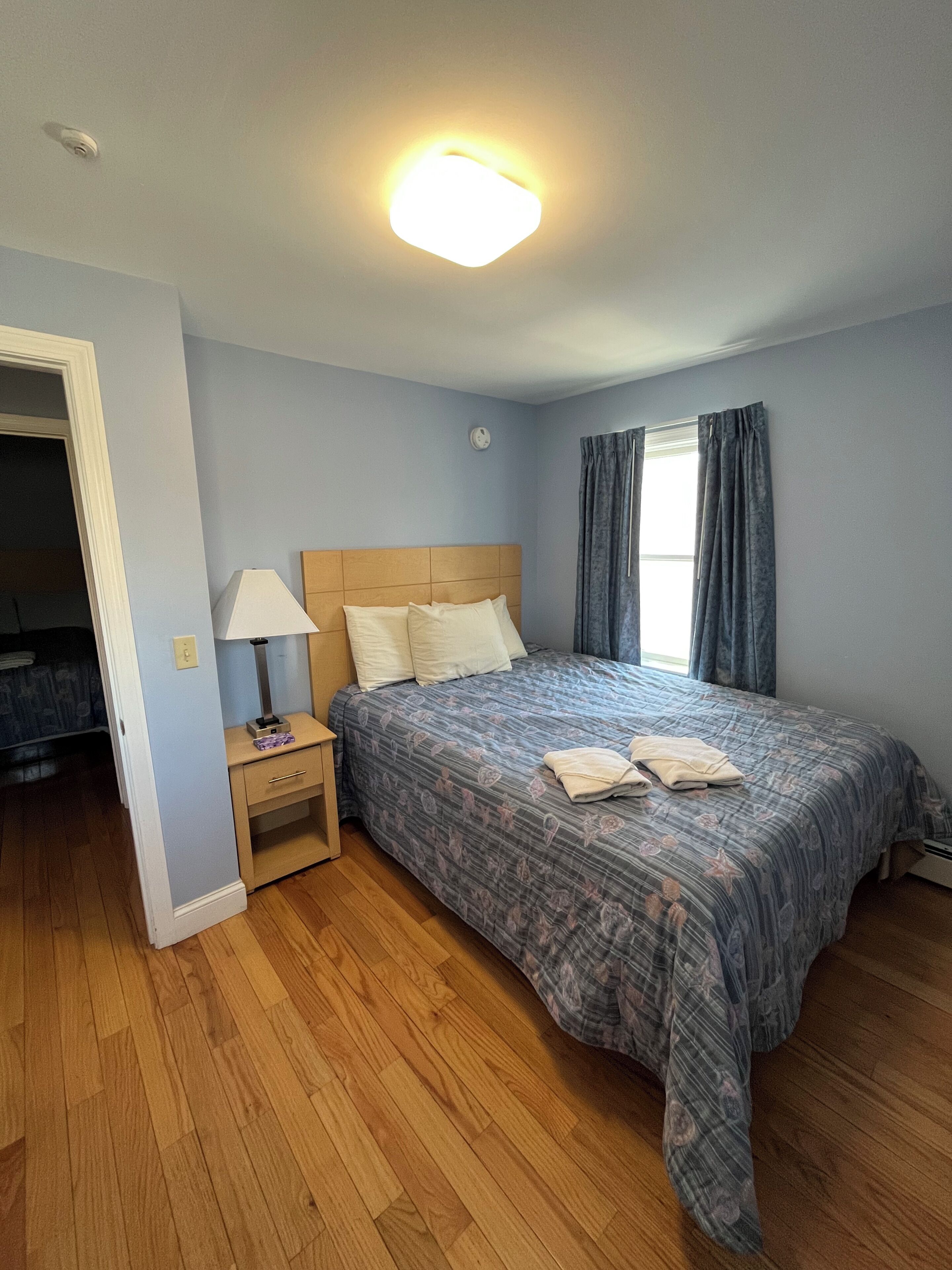 A bedroom with a bed, nightstand, lamp, and a window with curtains.