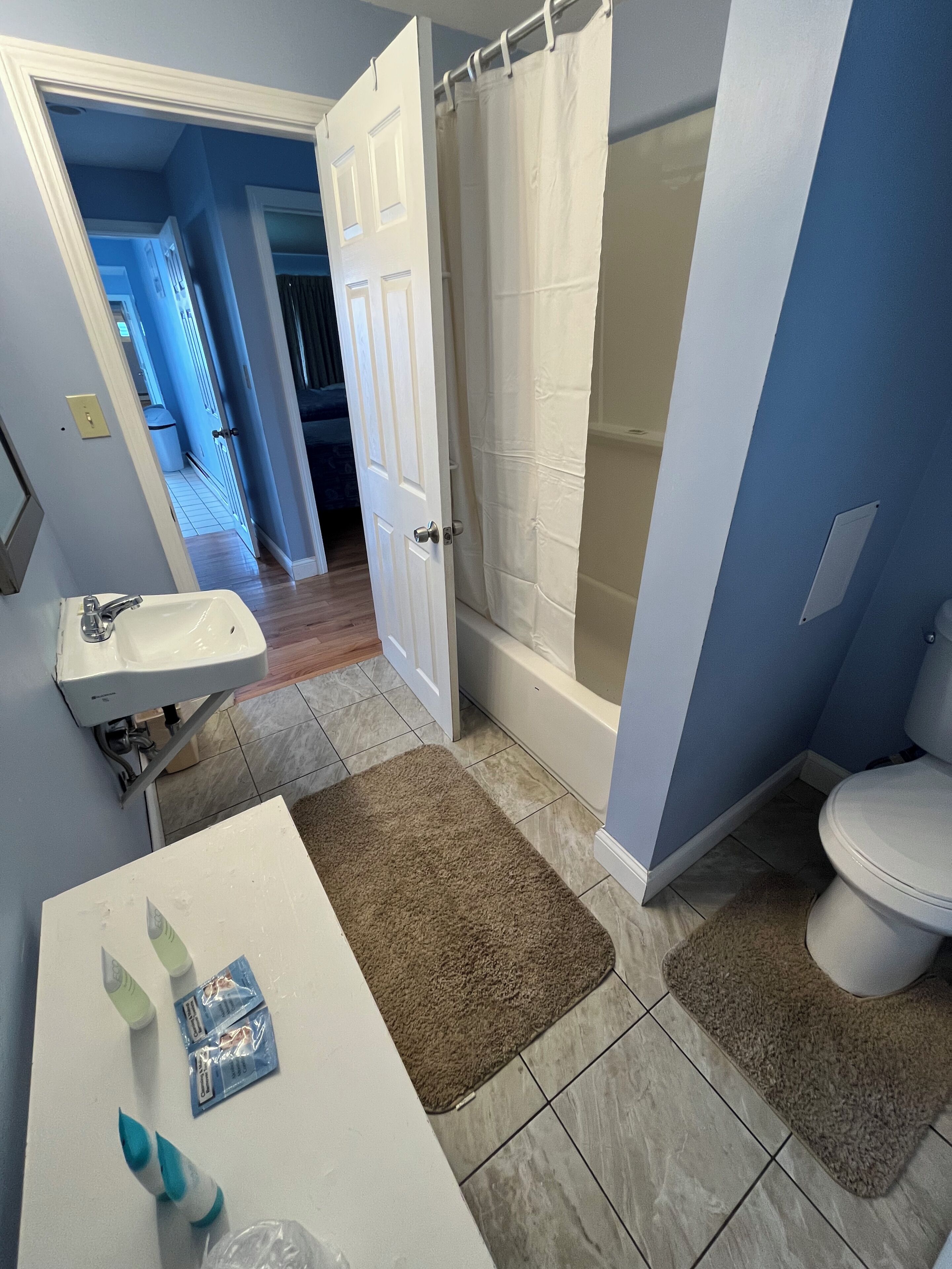 Une salle de bain avec un lavabo blanc, une baignoire et des toilettes. Il y a des tapis marron sur le sol.
