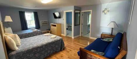 A room with two beds, a wooden bench, a TV, and a door leading to another room.