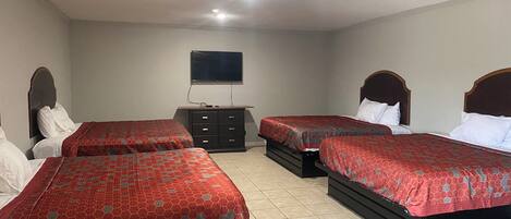 A hotel room with three beds, a TV on the wall, and a dresser.
