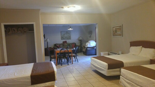 A hotel room with two beds, a dining area with chairs and a table, and a desk with a lamp.
