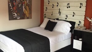 A bedroom with a bed, a nightstand, a painting, and a wall with musical notes. - Pascagoula Extended Stay (Pascagoula)