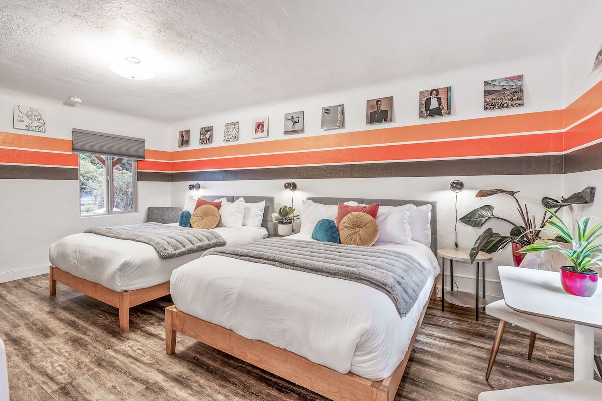 A bedroom with two beds, a small table, and a potted plant.