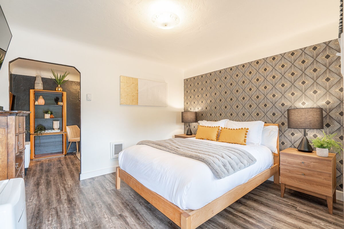 A bedroom with a wooden bed, a nightstand with a lamp, a dresser, and a mirror.