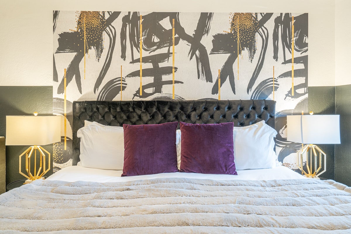 A bed with a tufted headboard, two white pillows, and two purple pillows.