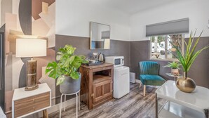 Una cocina moderna con microondas, un mueble de madera, un refrigerador pequeño, un sillón verde azulado y una planta en maceta.