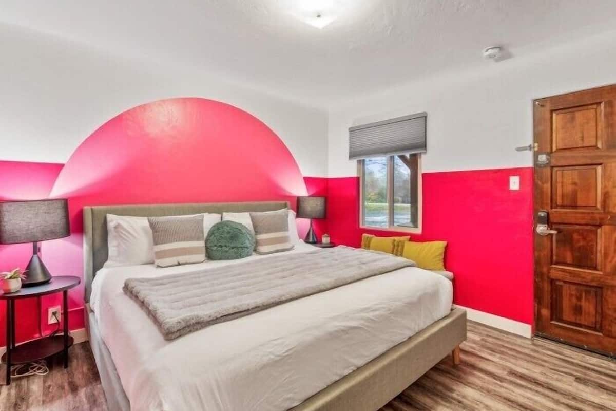 A bedroom with a large bed, a wooden door, and a window with blinds.