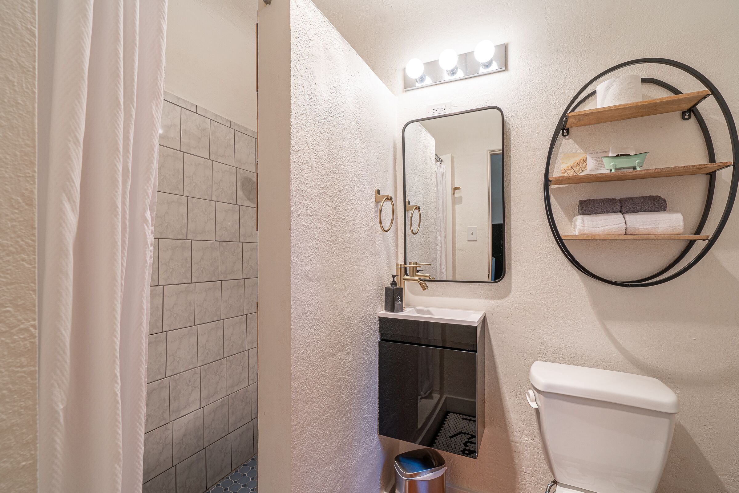 Un baño con ducha, lavabo, inodoro y espejo con luces arriba.