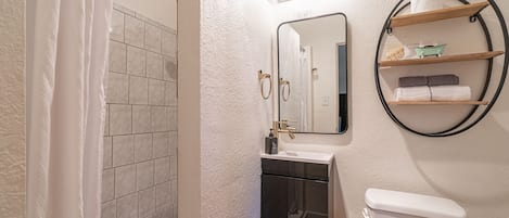 Un baño con ducha, lavabo, inodoro y espejo con luces arriba.