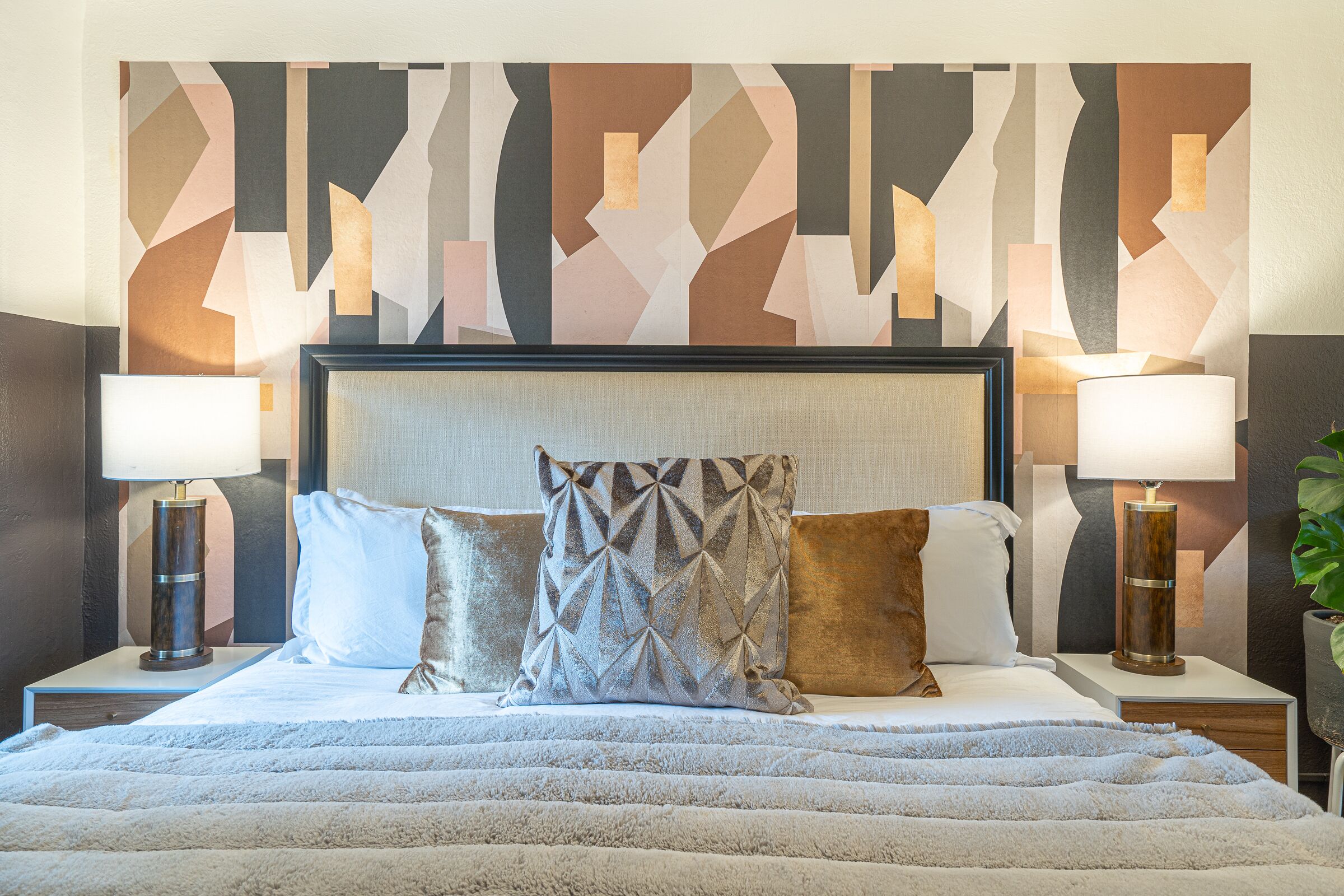 A hotel room with a large bed, two bedside tables, and a geometric-patterned wall.