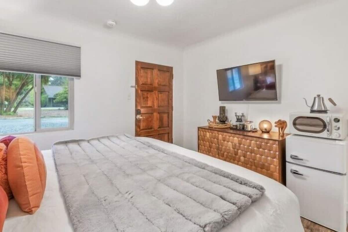 A bedroom with a bed, a wooden wardrobe, a television, and a kitchenette.