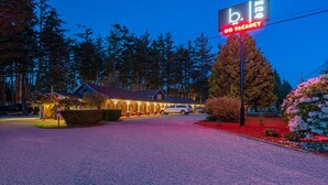 Un hotel con un letrero iluminado que indica habitaciones agotadas, rodeado de árboles y un jardín cuidado.