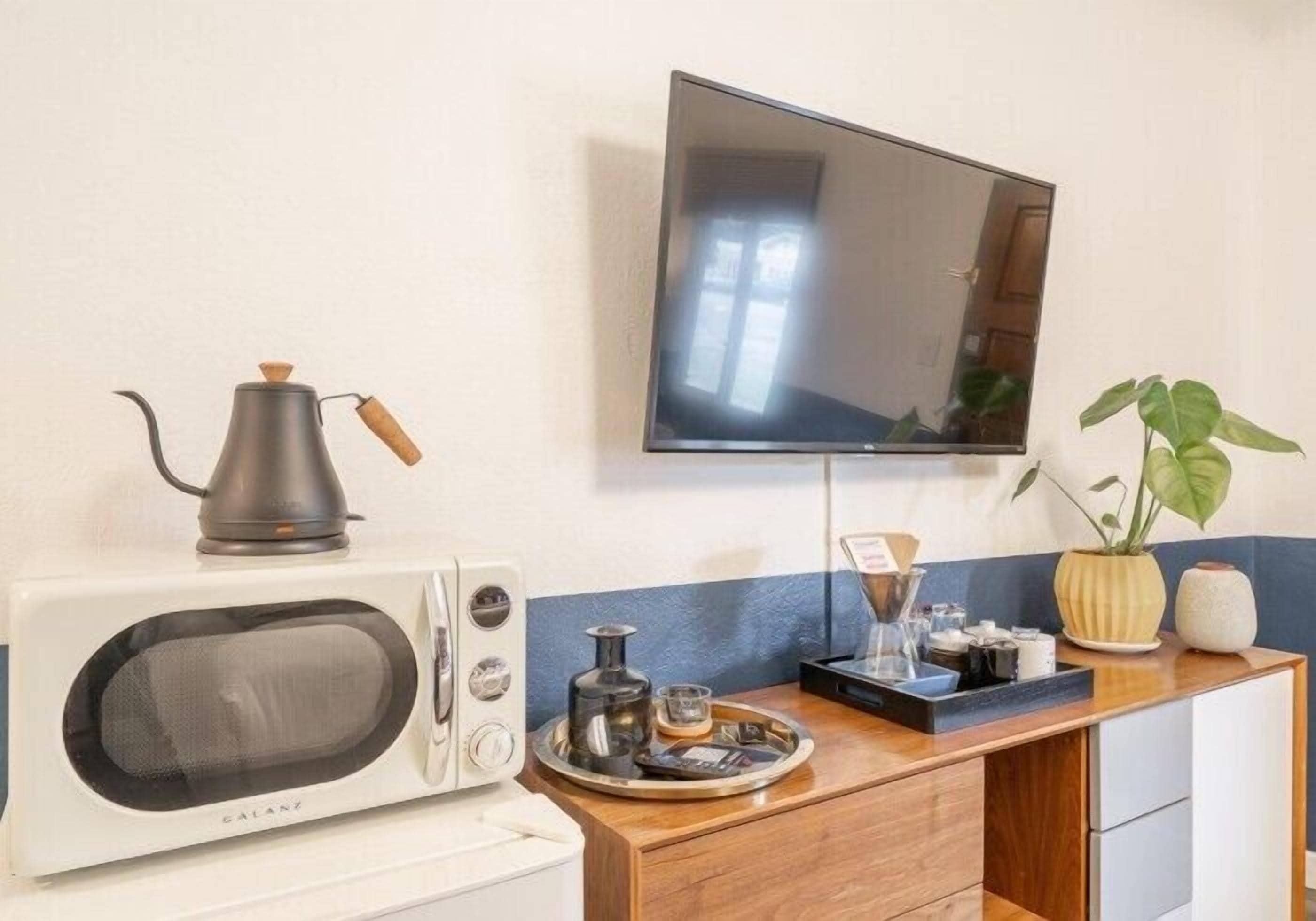 Una kitchenette con microondas, cafetera y una bandeja con té y azúcar. Un televisor está montado en la pared sobre la encimera.