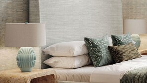 Un dormitorio con cama, almohadas, una lámpara y un florero.