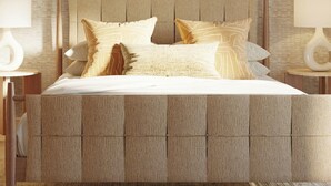 Una cama con cabecera texturizada, dos mesitas de noche con lámparas y un cuadro en la pared.