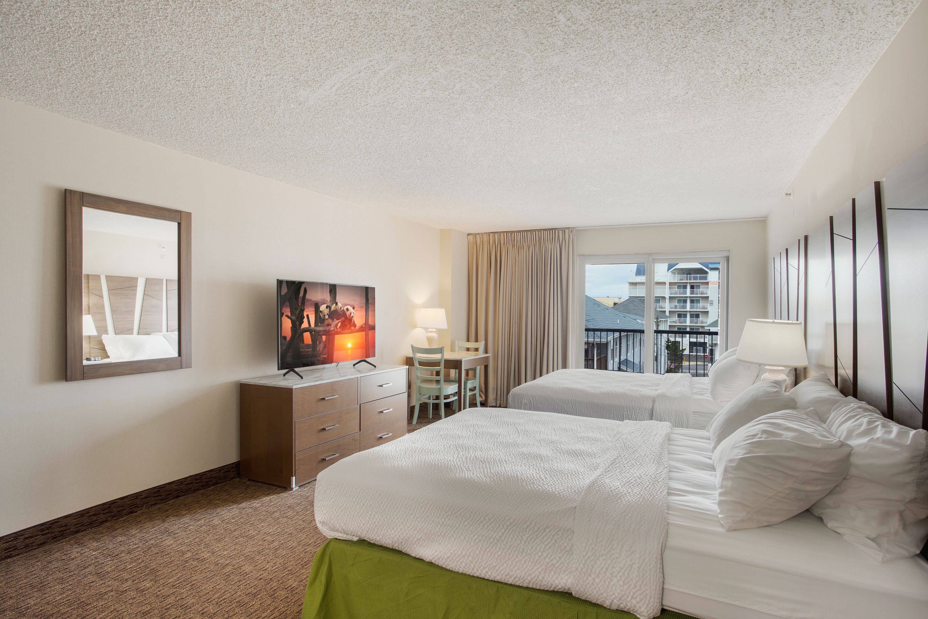 Een hotelkamer met twee bedden, een bureau, een stoel, een televisietoestel en een raam met uitzicht op gebouwen.