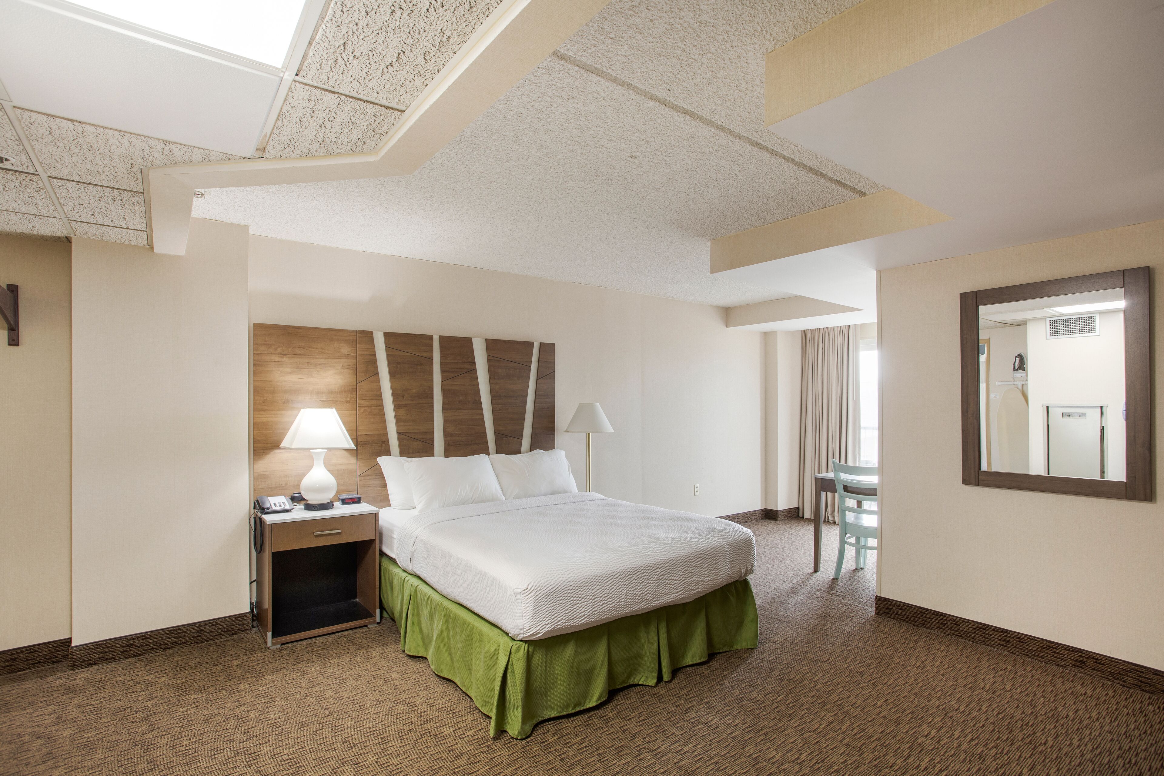 Una habitación de hotel con cama, mesita de noche, lámpara, sillón y espejo.
