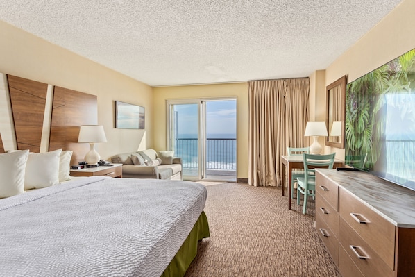 A hotel room with a large bed, a desk, a chair, a television, and a view of the ocean through the sliding glass door. - The Americana Hotel (Ocean City)