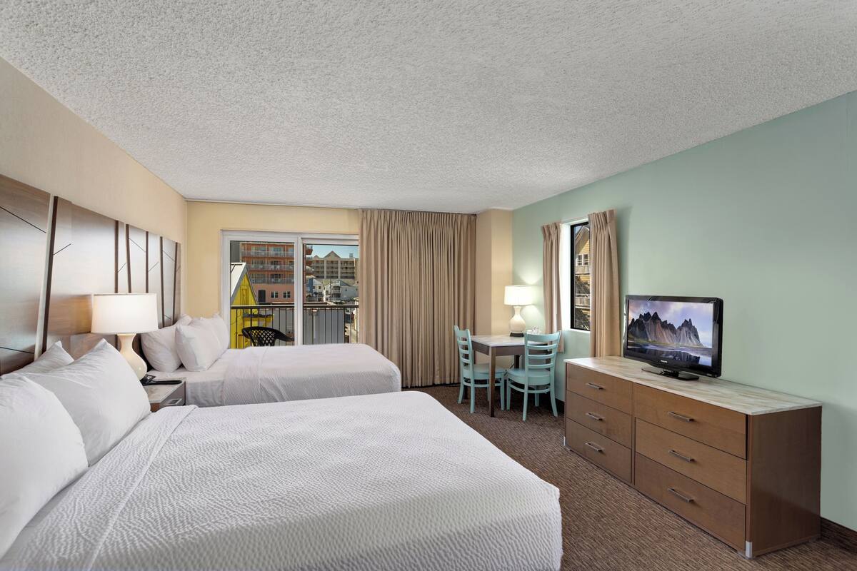 Een hotelkamer met twee bedden, een bureau met stoelen, een televisie en uitzicht naar buiten.