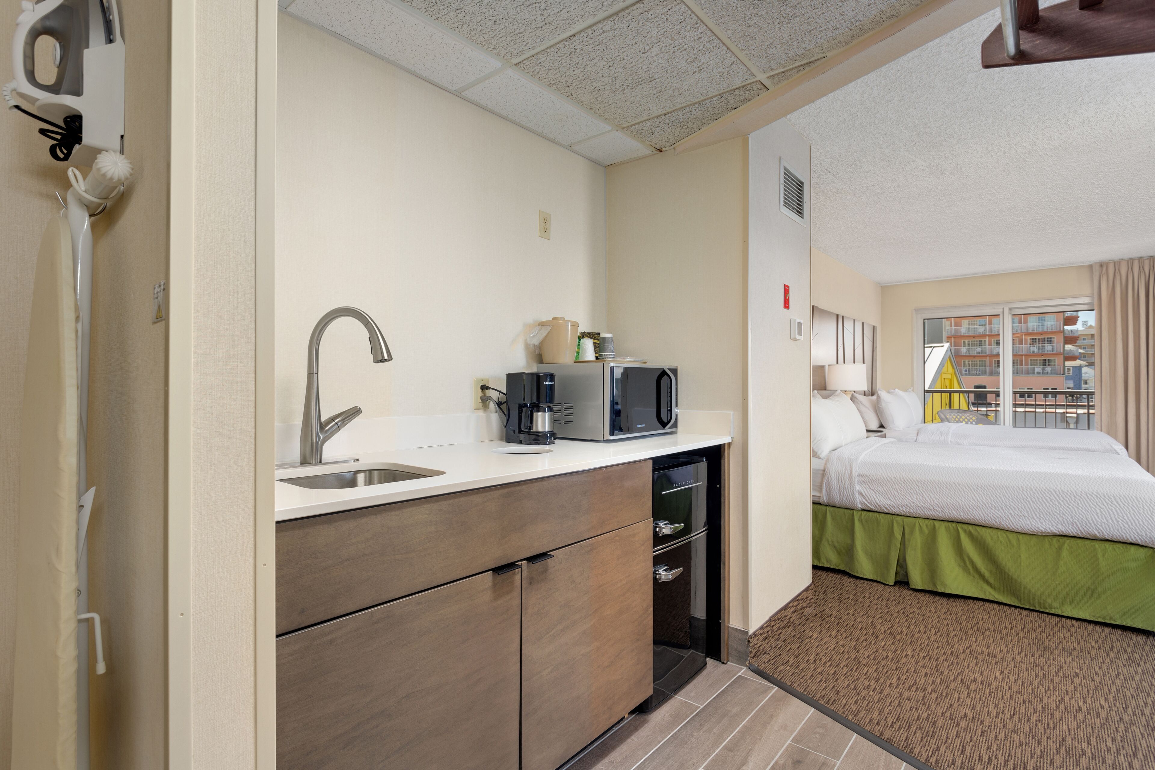 Habitación de hotel compacta con kitchenette, una cama y vistas de edificios a través del ventanal.