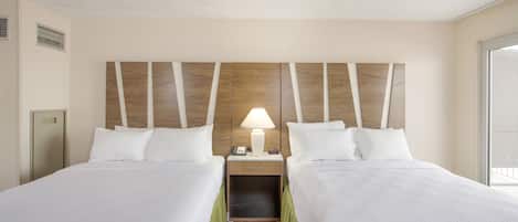 A hotel room with two beds, a nightstand with a lamp, a wooden headboard, and a window.