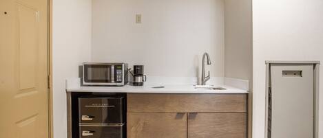 Una kitchenette compacta equipada con microondas, cafetera y lavamanos.