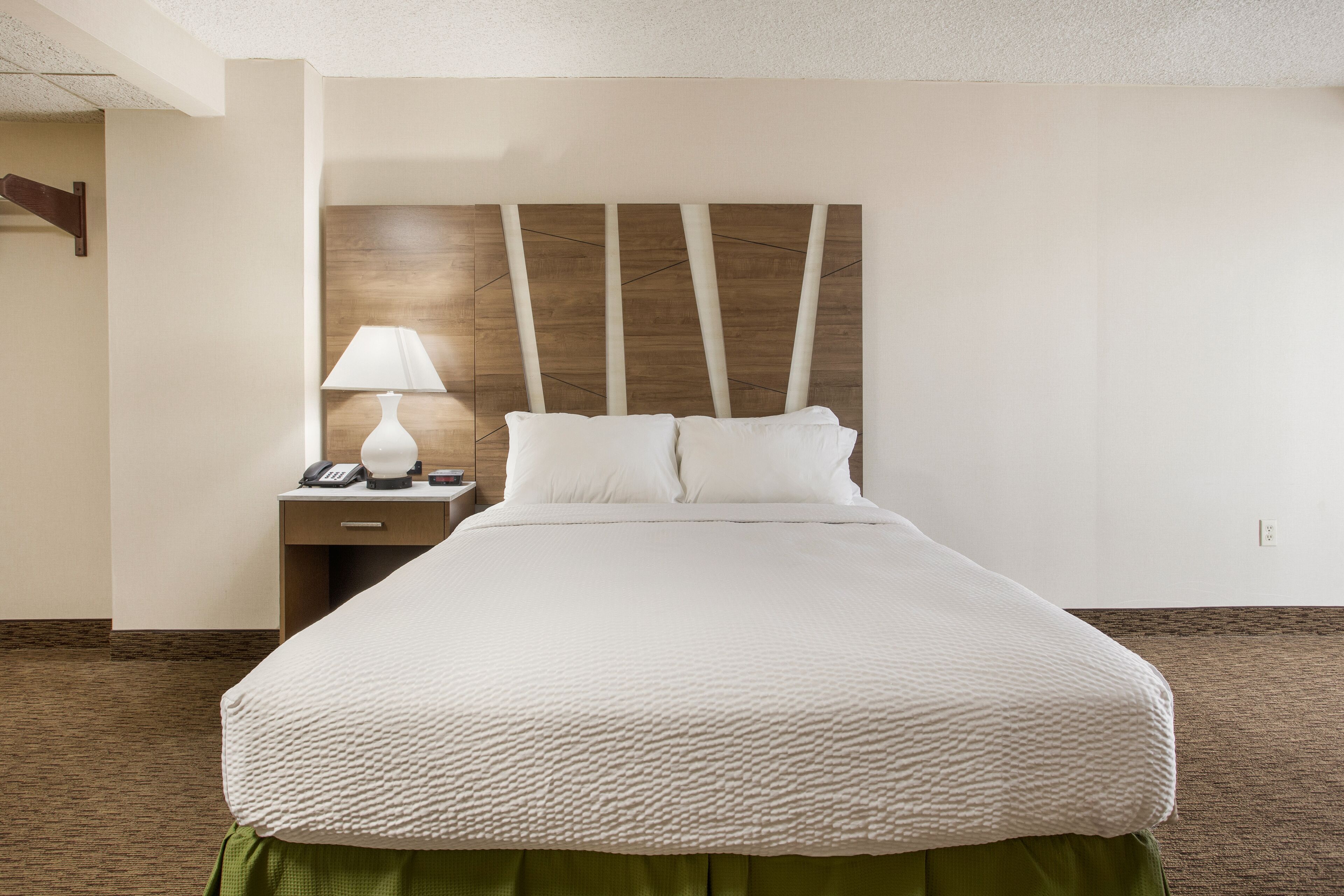 A neatly made bed with a white textured bedspread, a wooden headboard, and a bedside table with a lamp and phone.