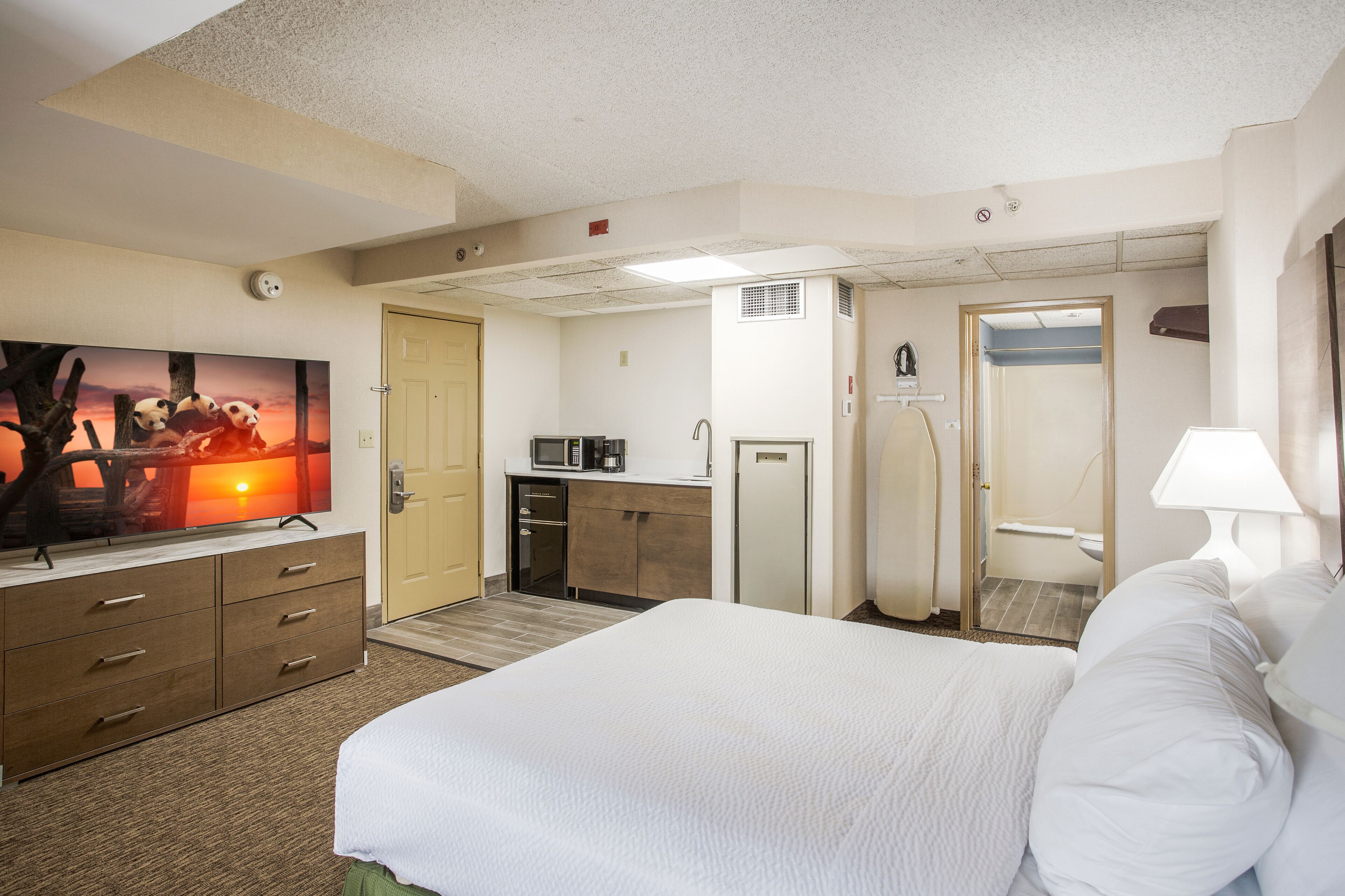 Ett hotellrum med en säng, en TV, ett skrivbord, en mikrovågsugn och en dörr som leder till ett badrum.