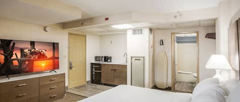 Habitación de hotel con cama, televisor, escritorio, microondas y puerta que da a un baño.