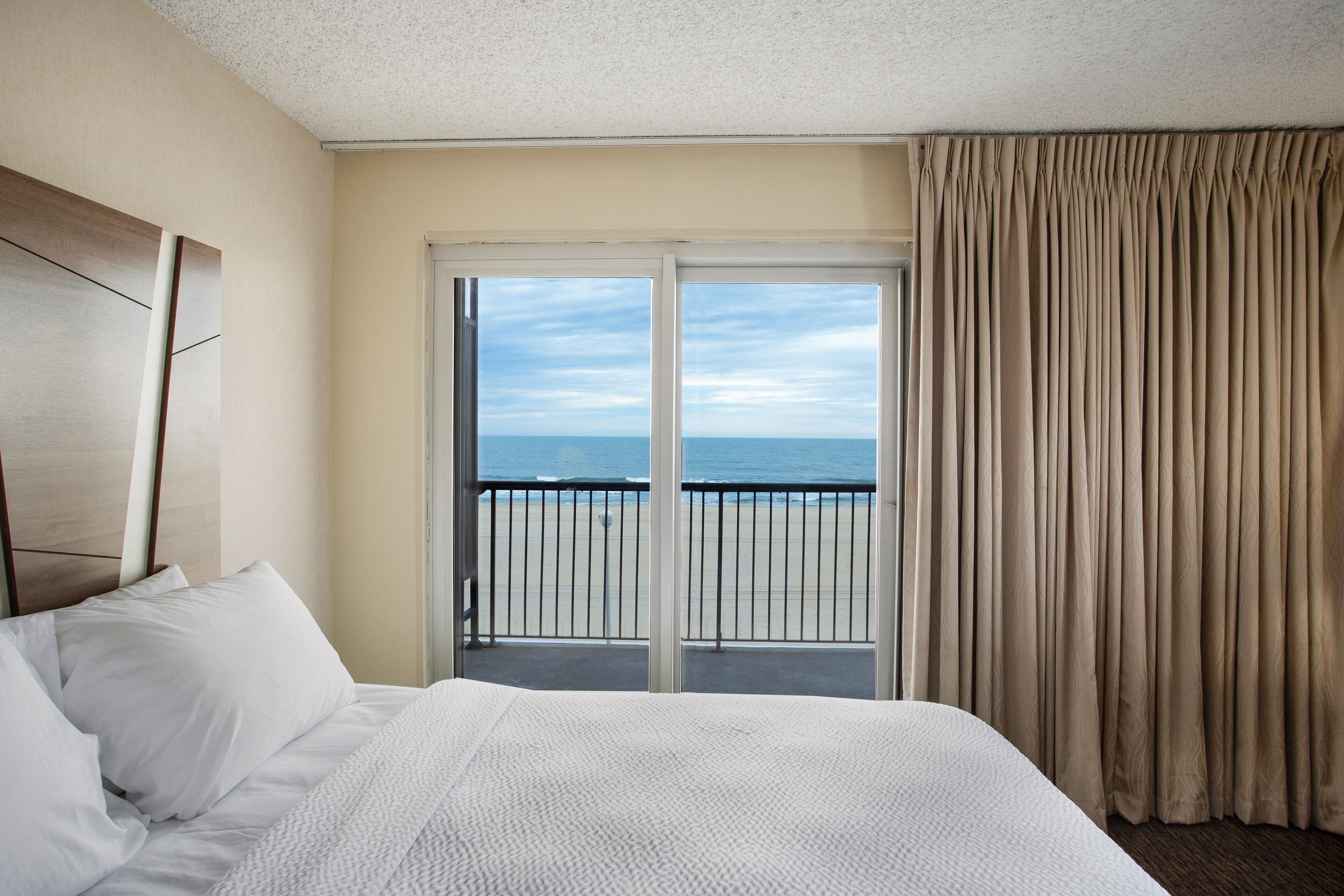 A hotel room with a bed, a view of the ocean through a sliding door, and a balcony with a railing.