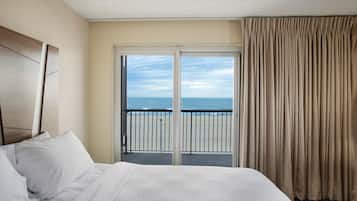 A hotel room with a bed, a view of the ocean through a sliding door, and a balcony with a railing.