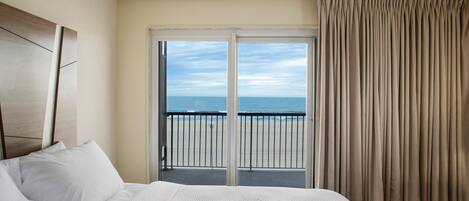 A hotel room with a bed, a view of the ocean through a sliding door, and a balcony with a railing.