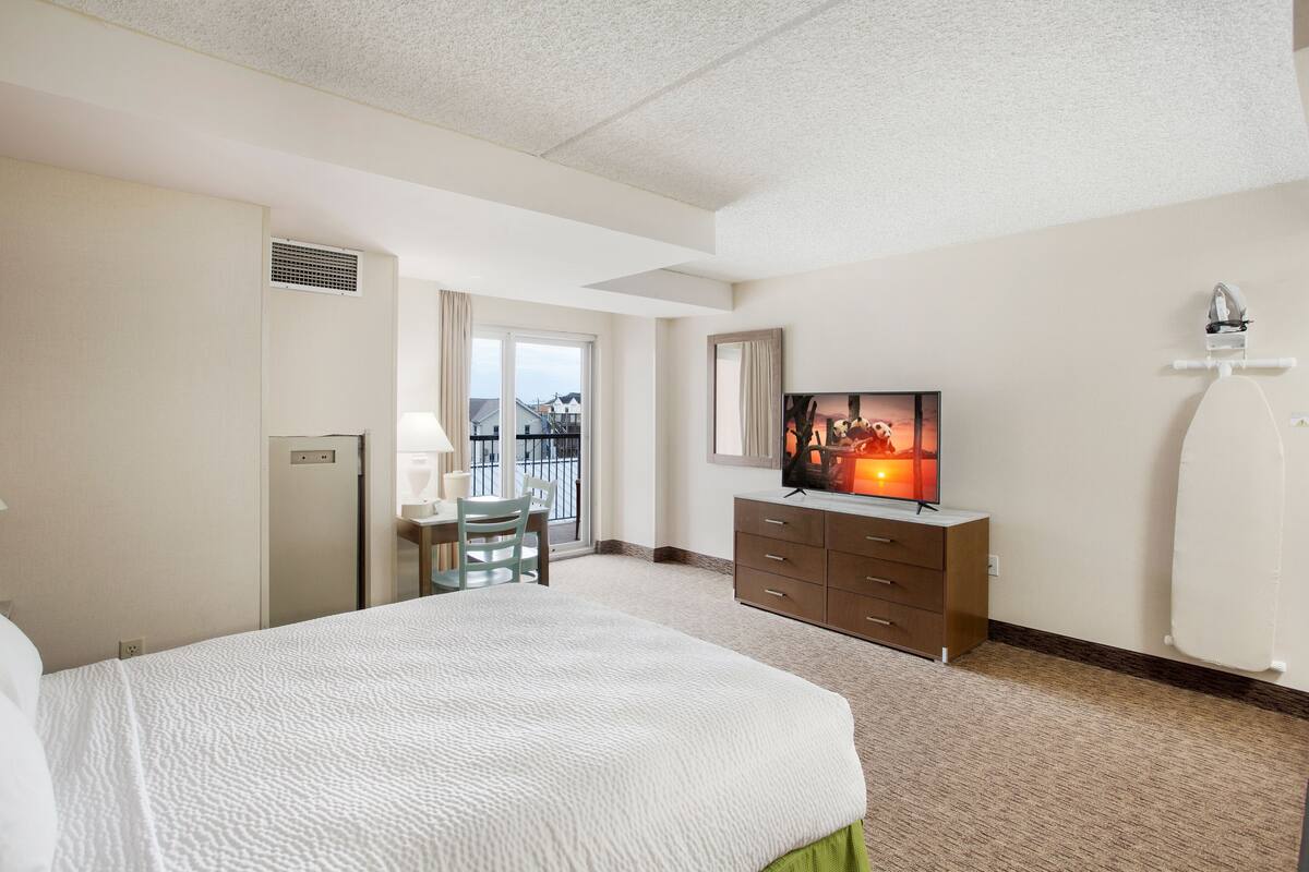 Hotelkamer met een groot bed, een televisie, een bureau met stoel en uitzicht buiten via een schuifdeur.