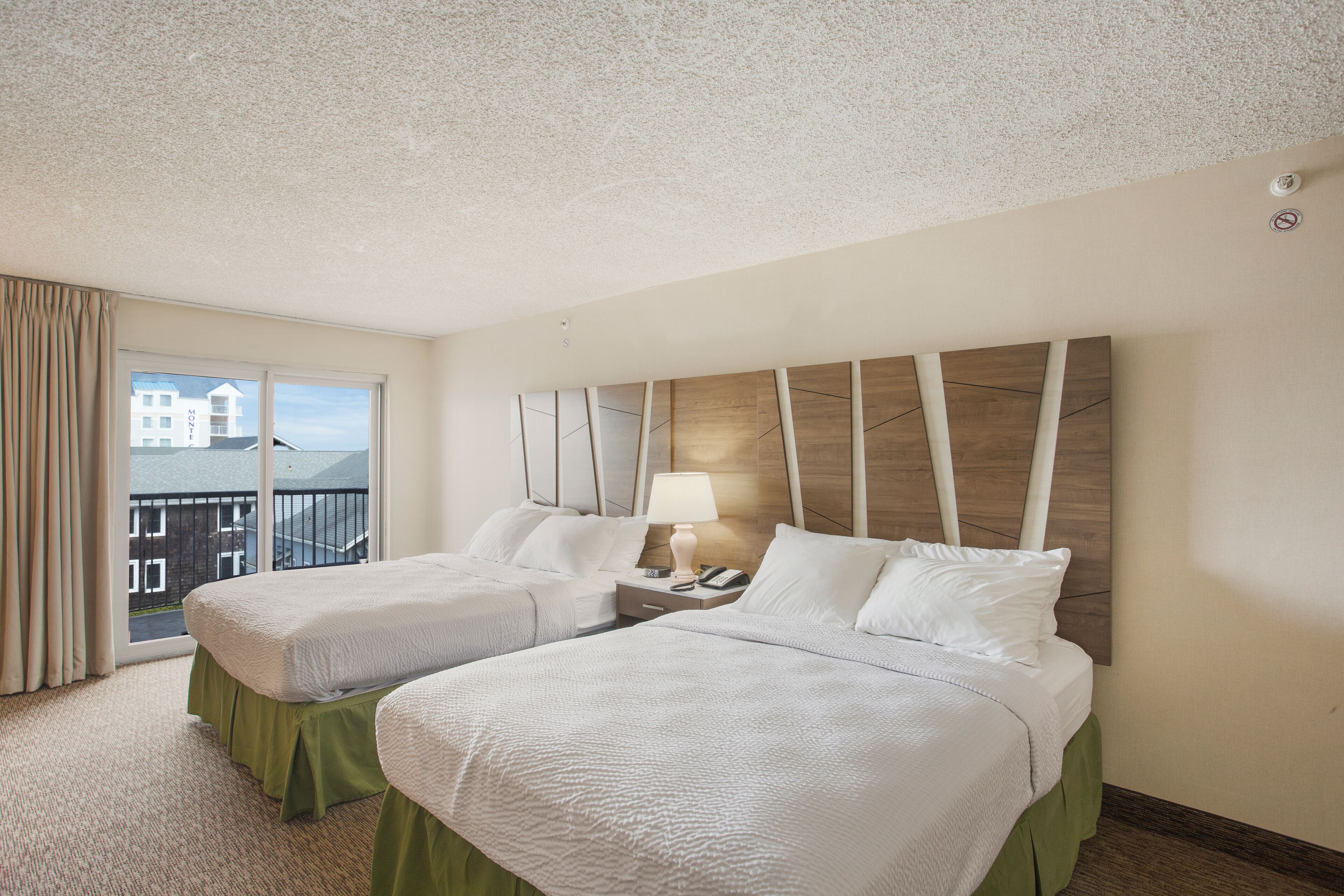 Habitación de hotel con dos camas, un balcón con vistas y un cabecero moderno.